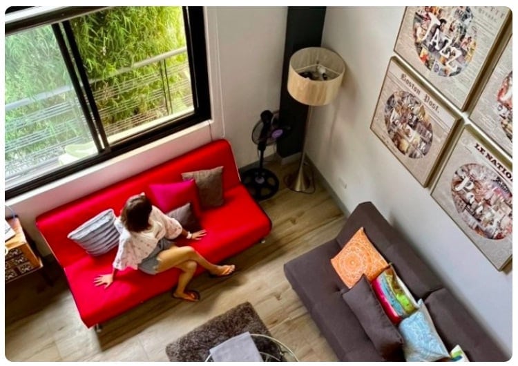 Accogliente soggiorno di un hotel con un bambino seduto su un divano rosso vicino a una grande finestra.