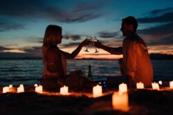 A couple toasts with wine glasses at sunset on a beach in Coron, surrounded by glowing candles, their day of island hopping and exploring Coral Gardens a perfect prelude to this romantic moment.