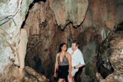 In the heart of Coron, a couple explores a rocky cave, surrounded by rugged stone walls. The woman wears a leopard print top and black shorts, while the man sports a white shirt. They both appear to be relishing their Palawan adventure.