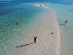 Aerial view of a narrow sandbar surrounded by clear turquoise water, with several people enjoying an island hopping adventure along the sandy path in Balabac.