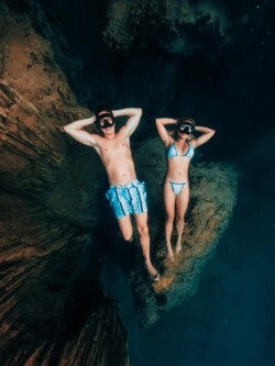 Free diving in Barracuda Lake. Two snorkelers float gracefully underwater near rocky formations in Palawan, wearing swimwear and masks with arms behind their heads, savoring the serene beauty as part of an island hopping adventure.