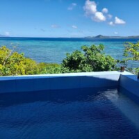 View of the ocean from the Sand Island main house pool. Tropical trees surround the property with a.