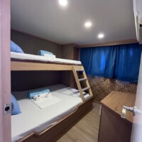 Bunk bed room with two beds, blue curtains, and wooden furniture on a dolphin-themed liveaboard. Per.