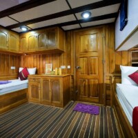 Interior of a wooden cabin on Siren Liveaboard with two single beds and colorful pillows.