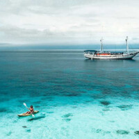 Siren Liveaboard sailing in clear blue Philippine waters with a kayaker nearby.