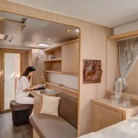 Modern hotel room with a woman working at a desk and a comfortable bed.