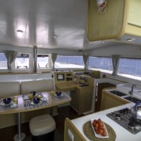 Luxury yacht interior with dining area and kitchen, overlooking the sea.