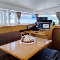 Interior of a boat with a table, computer, and scenic ocean view.