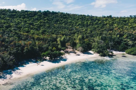 Beach with dense forest, calm sea, and boats near Galoc Island.