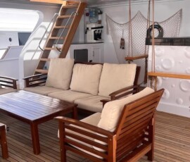 Relaxing yacht lounge featuring wooden furniture, beige cushions, and marine-themed decor. Seating area on luxury yacht with wooden sofas and nautical decorations in Philippines.