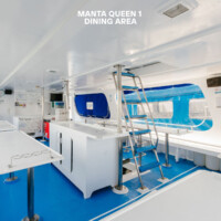 Relax in the Manta Queen 1 dining area featuring modern white furnishings and vibrant blue details, perfect for onboard dining experiences. Manta Queen 1 dining area with bright white interior and blue accents, offering a comfortable space.