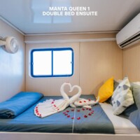 Comfortable cabin with double bed, towel swans, and romantic rose petals, perfect for a relaxing stay. Double bed with towel swans and rose petals in a cozy cabin.