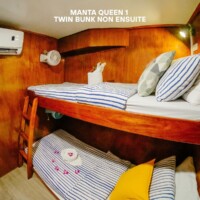 Comfortable twin bunk beds with striped bedding in a wooden cabin, perfect for island hopping trips. Bunk bed in a cozy cabin on the Manta Queen 1 cruise ship in the Philippines.