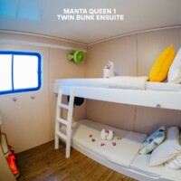 This image shows a cozy twin bunk bed with an ensuite bathroom in Manta Queen 1, featuring a bright window, colorful pillows, and a clean, modern desi. Bunk bed with twin mattresses and private bathroom in a compact, modern cabin. Bright window and col.