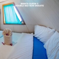 Comfortable double bed in a cozy hotel room in the Philippines, featuring a small window with blue curtains. Cozy double bed in a Philippine hotel room with a small window and blue curtains.