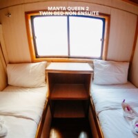 Cozy twin bed cabin on the Manta Queen 2 cruise, featuring a window and elegant wooden interior. Twin bed cabin on Manta Queen 2 cruise ship with window view.