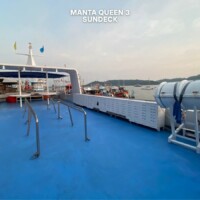 The sundeck of the Manta Queen 3 cruise ship offers a relaxing space with safety gear and beautiful views of the surrounding waters. Manta Queen 3 cruise ship sundeck with safety equipment and scenic water view.