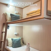 Cozy twin bunk cabin with wooden interior, pillows, and a towel sculpture. Ideal for budget travelers. Bunk bed in a compact cabin on the Manta Queen 3 cruise ship.